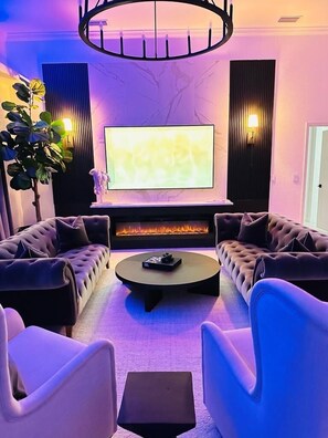 Een moderne woonkamer met een open haard, een grote flatscreen televisie en comfortabele zitmogelijkheden.