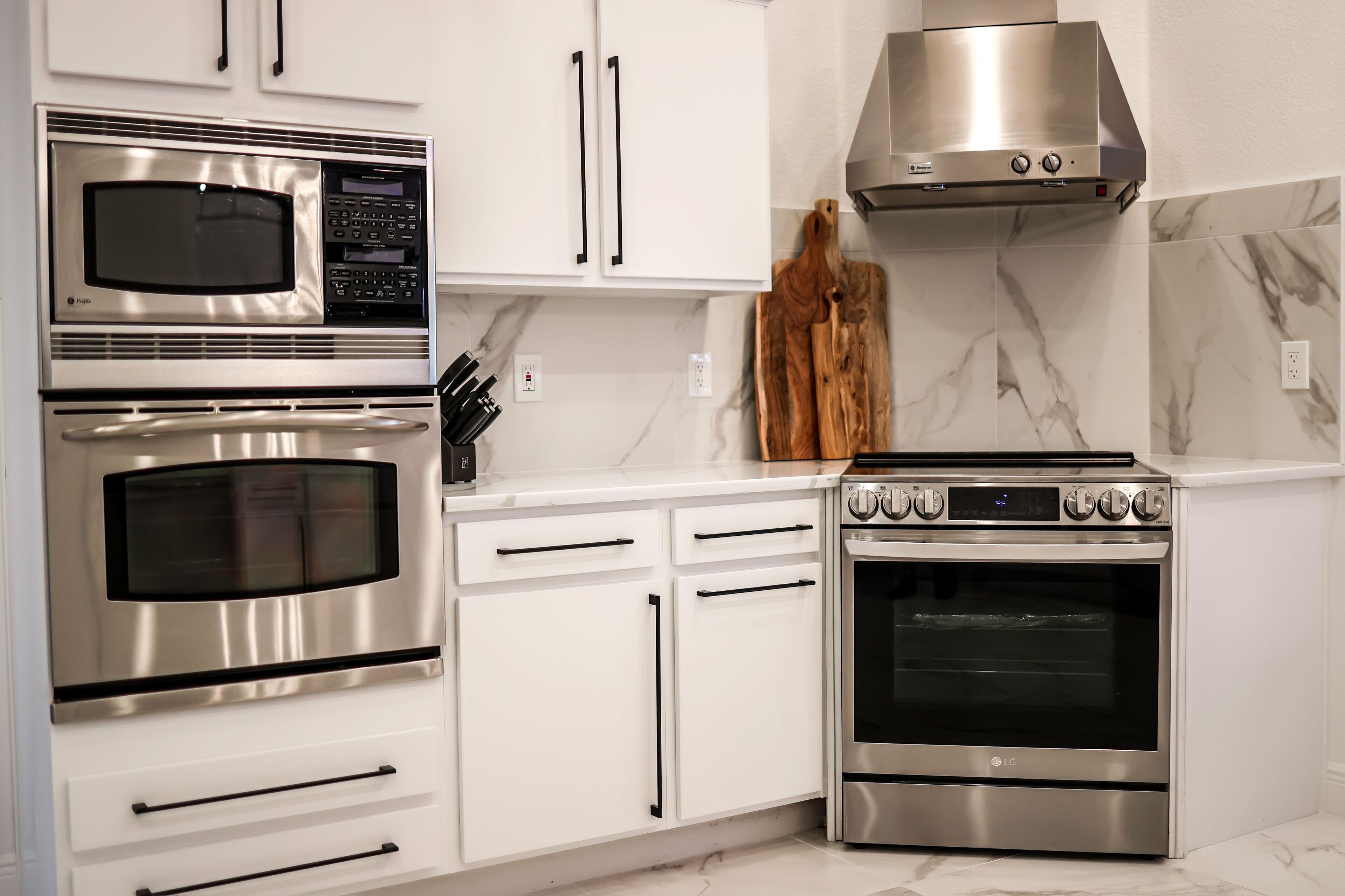 Een moderne keuken met roestvrijstalen apparatuur, witte kasten en een marmeren achterwand.