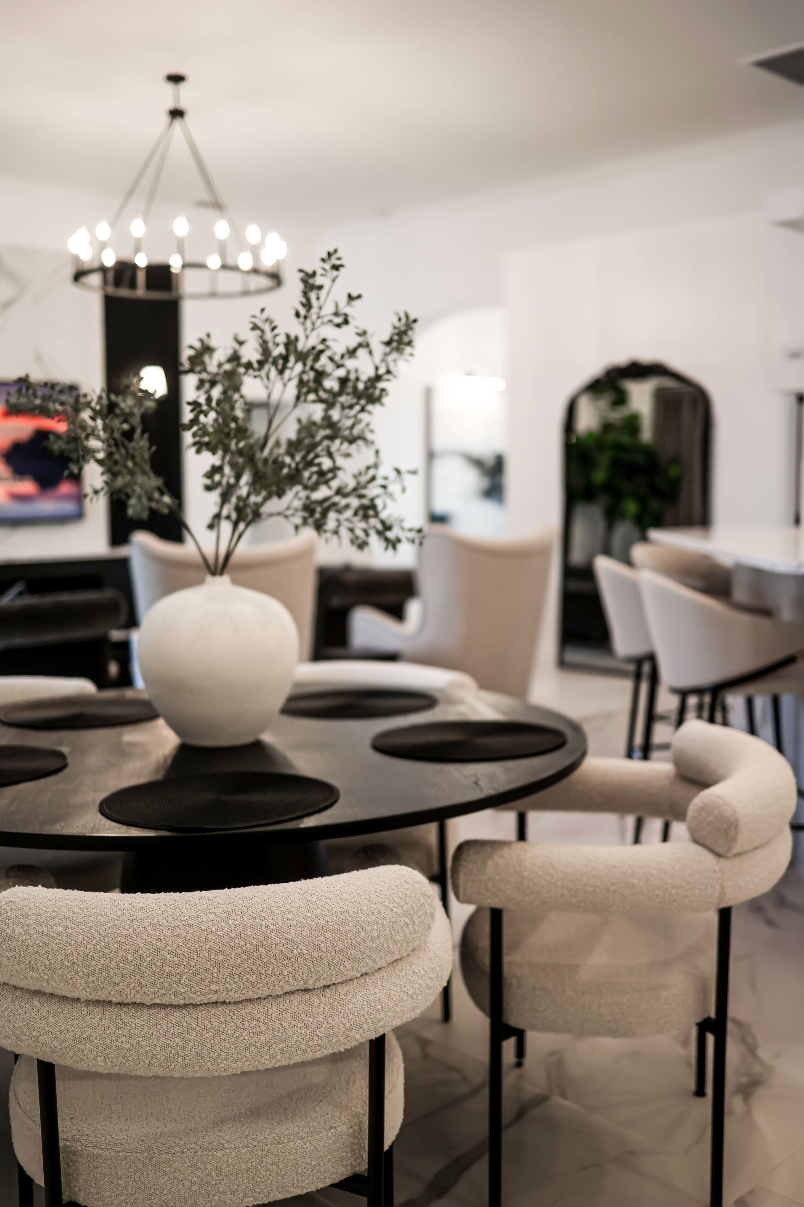 A modern dining area with a round table, white chairs, and a white vase with branches.