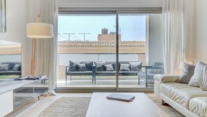 A modern living room with a sofa, a coffee table, and a balcony with a view of buildings. - Stunning 4 bed penthouse, direct acess to rooftop pool with 360o views of Port (Pollença)
