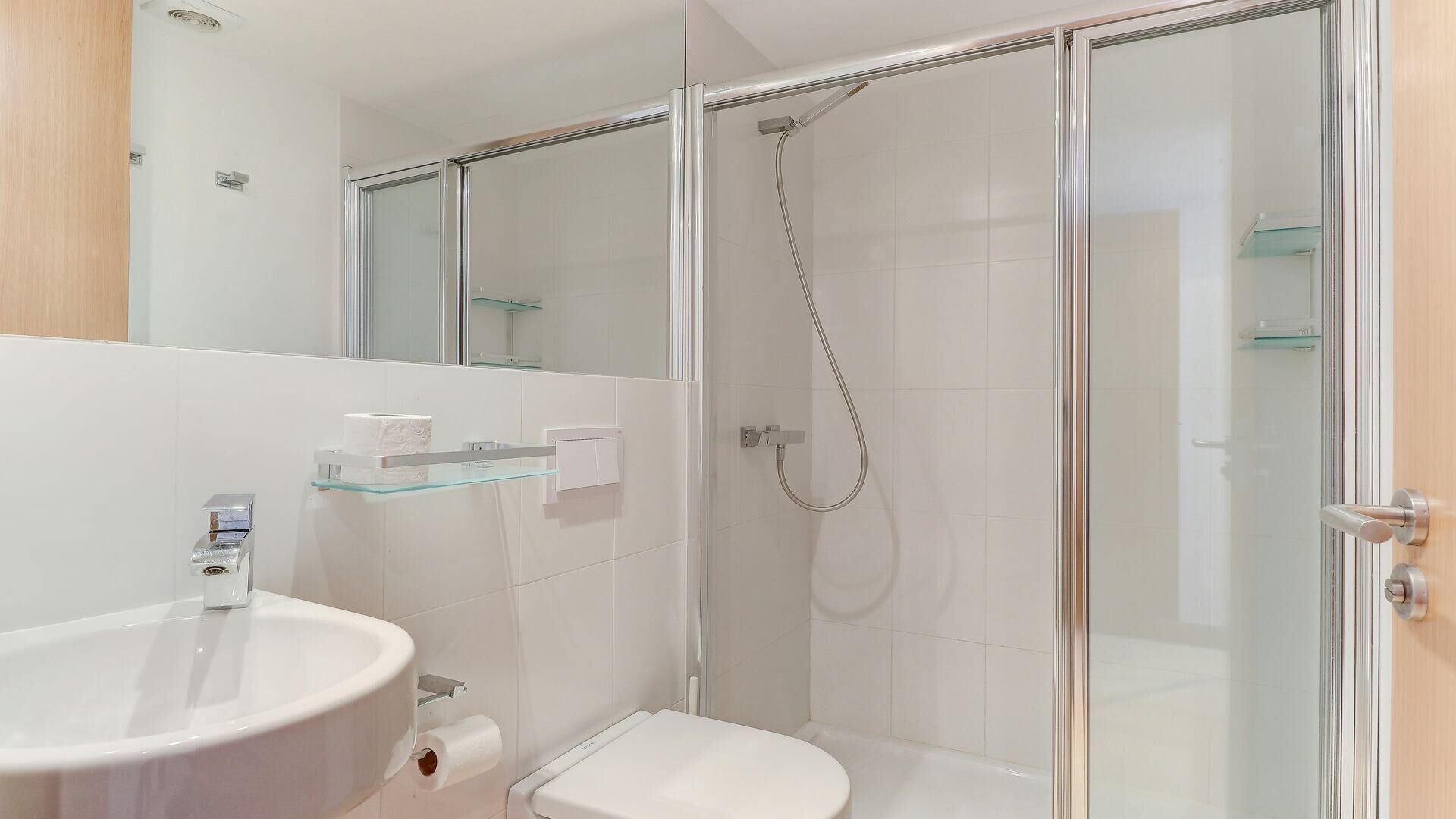 A modern bathroom with a glass shower enclosure, a toilet, and a sink with a glass shelf above it.