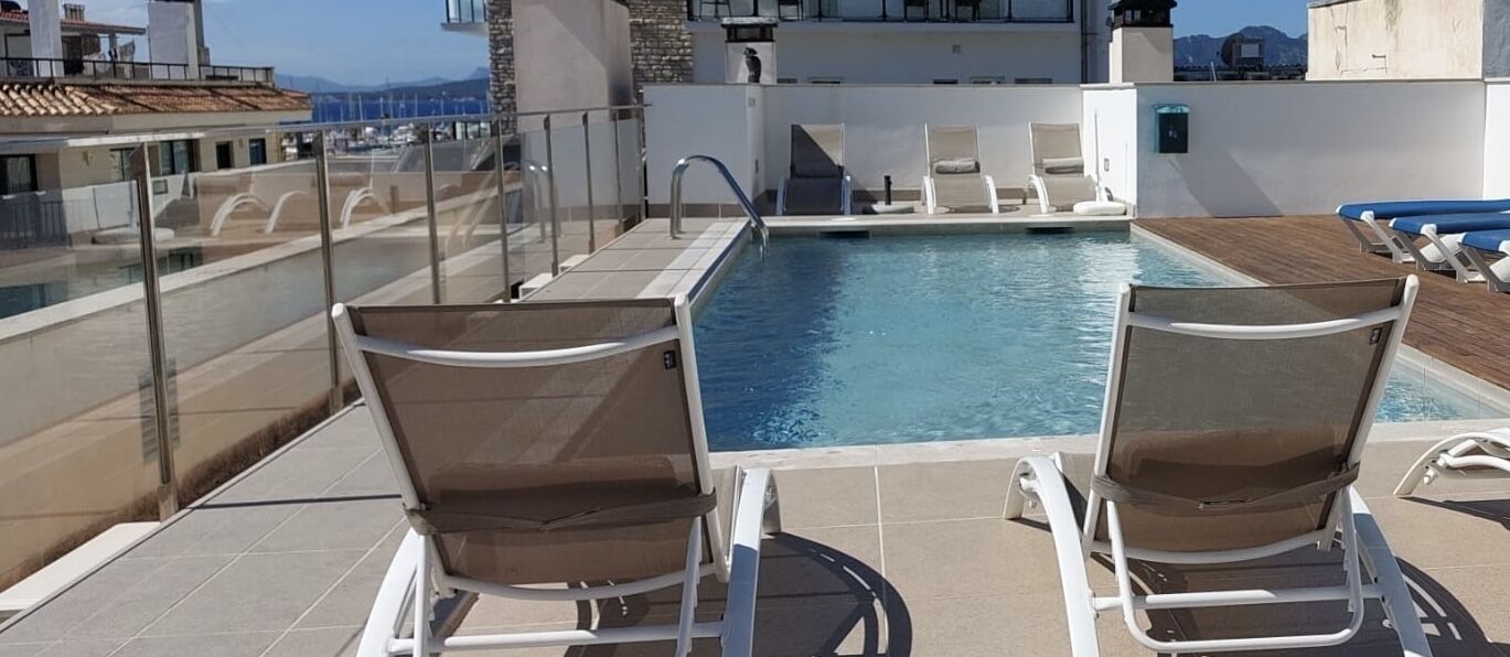A rooftop pool with two lounge chairs and a glass balustrade.