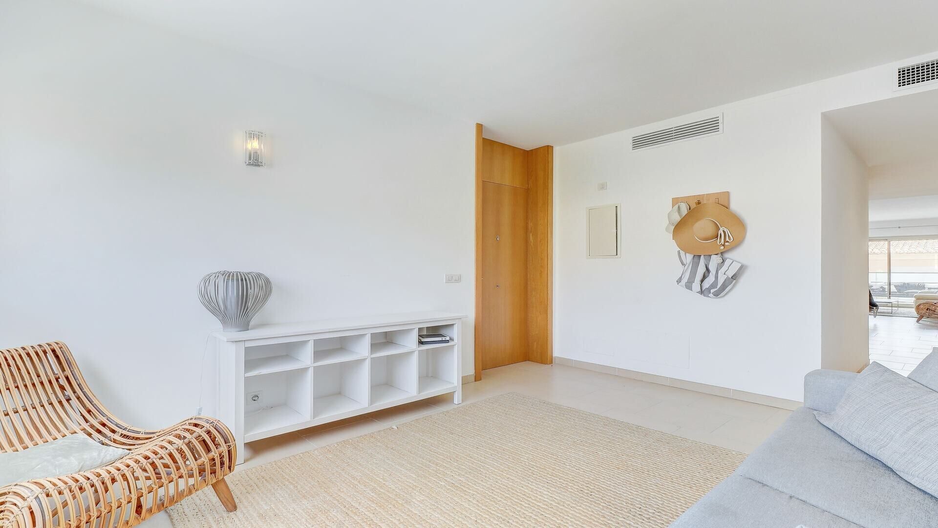 Un salon moderne avec une console blanche, des meubles en osier et un canapé gris.