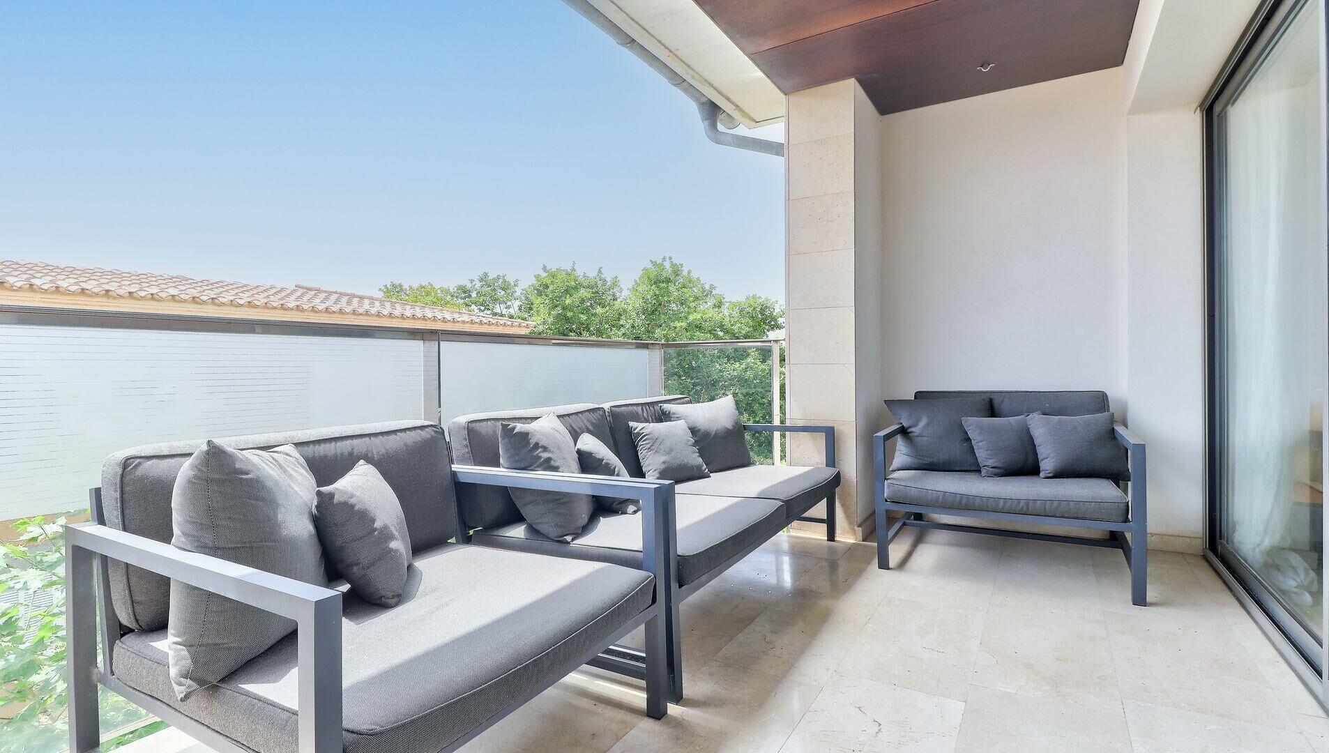 A balcony with a sofa and a chair, a glass door, and a view of greenery.