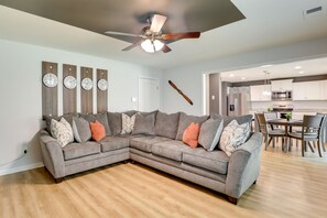 A modern living room with a sectional sofa, a ceiling fan, and a dining area with a kitchen in the background. - 'Vibe Villa' w/ Backyard ~ 8 Mi to Shaw AFB! (Sumter)