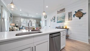 Une cuisine moderne dotée d’un grand îlot central, d’appareils électroménagers en acier inoxydable, de luminaires suspendus et d’une décoration sur le thème de la marine.