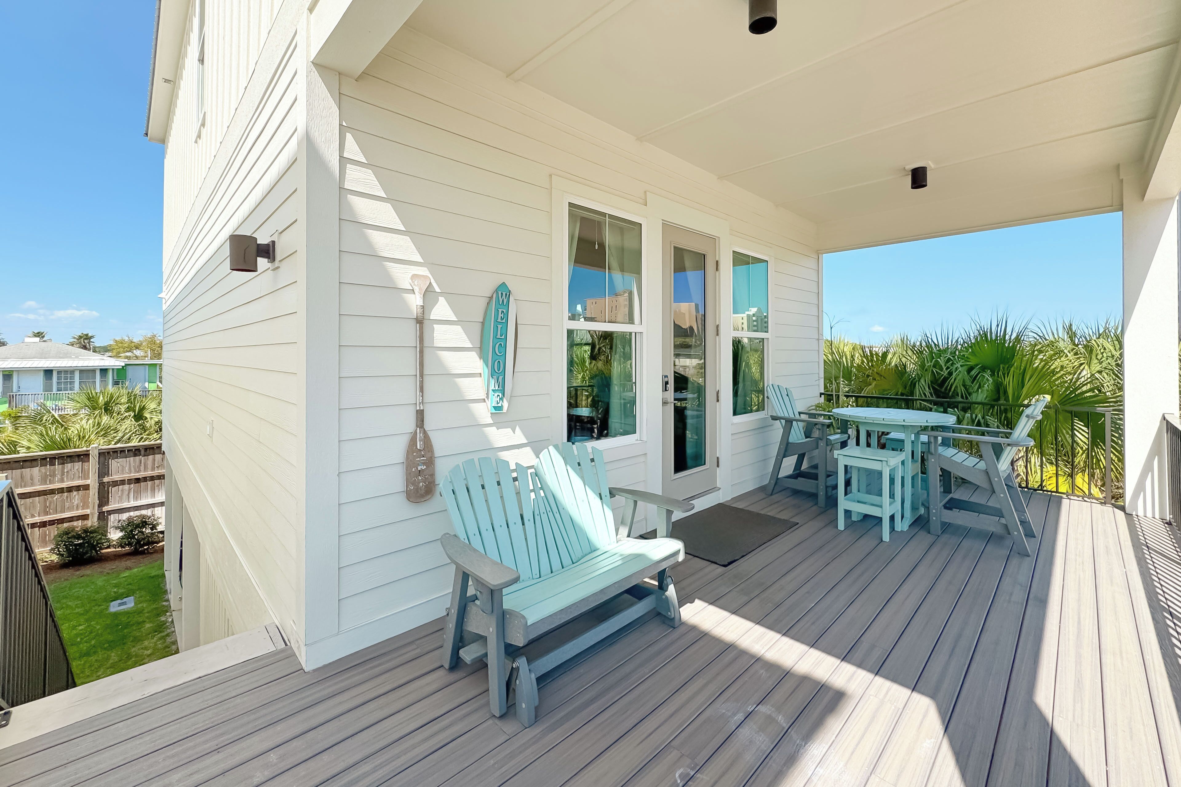 A covered porch with a bench and table, a 'WELCOME' sign, and a view of the backyard.