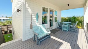 Un porche abrité avec un banc et une table, une pancarte indiquant « BIENVENUE » et une vue sur le jardin arrière.
