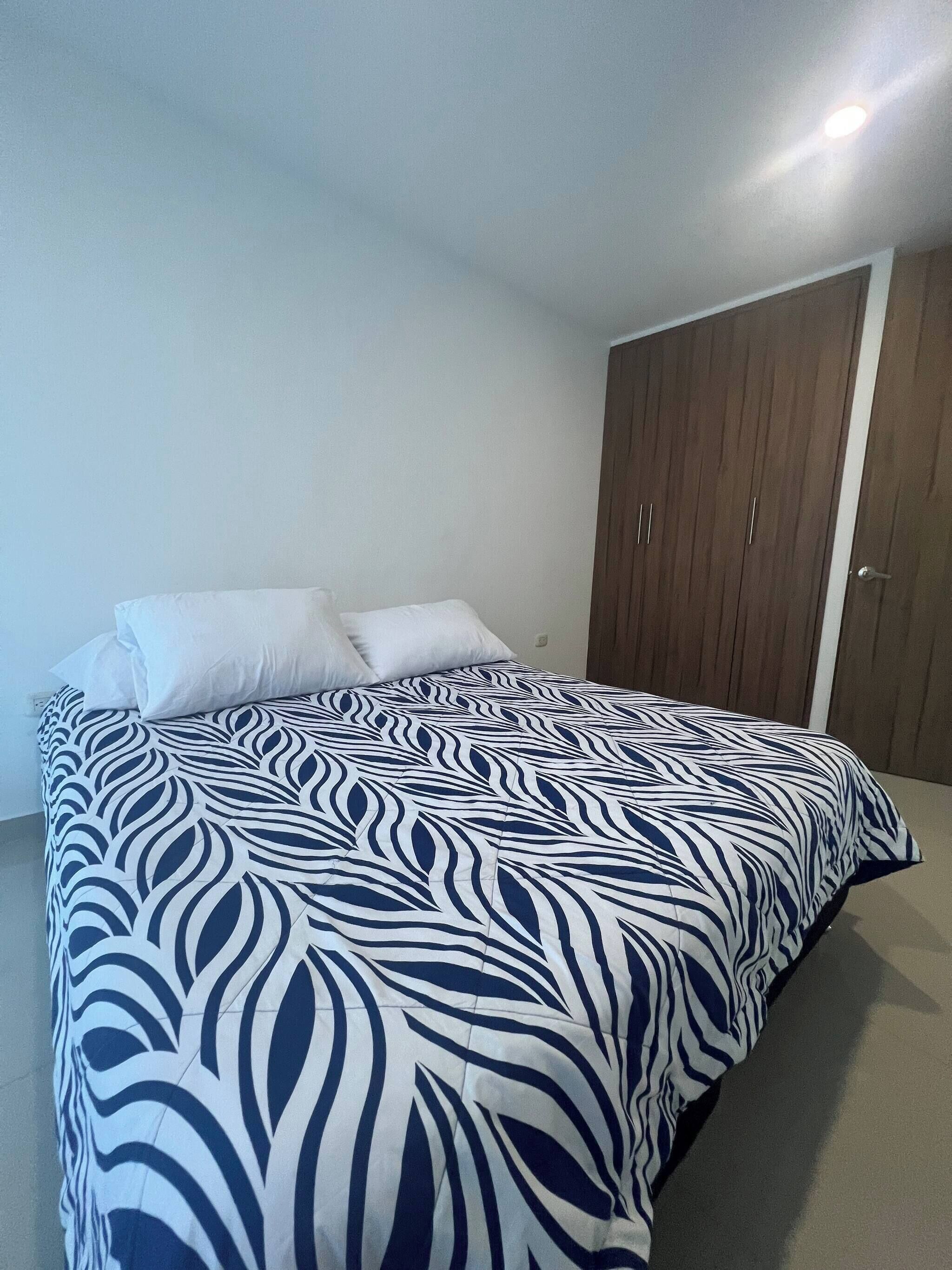 A bedroom with a bed, white pillows, a patterned bedspread, and a wooden wardrobe.