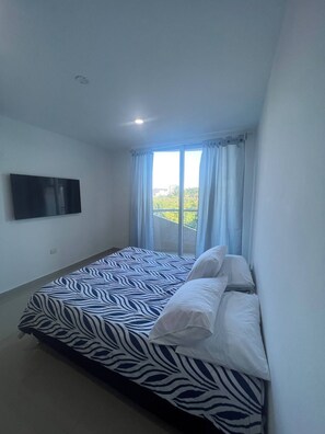 Un dormitori amb un llit, televisió de pantalla plana i una finestra amb cortines.