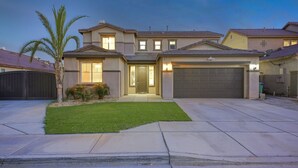 A two-story house with a front garage, a well-maintained lawn, and a palm tree.