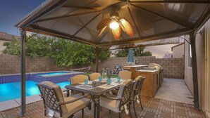 An outdoor patio with a pool, a covered dining area, and a barbecue station.