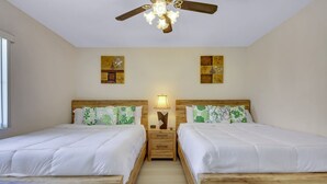 A double room with two beds, wooden headboards, a nightstand between the beds, a ceiling fan, and two wall-mounted artworks.