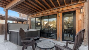 An outdoor patio with a hot tub, wooden chairs, and a table. - Impressive, brand new modern residence in Whitefish. Close to downtown, lake and ski bus! (Whitefish)