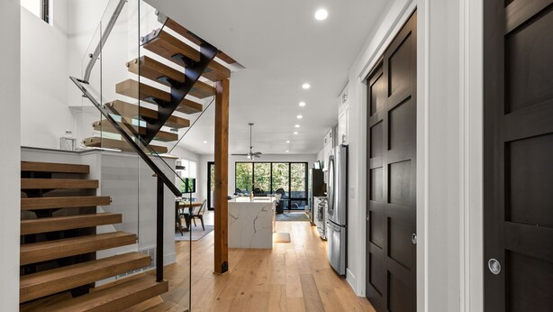 A modern kitchen with dark wooden cabinets, a central island, and a staircase with glass railings leading to an upper level. - Impressive, brand new modern residence in Whitefish. Close to downtown, lake and ski bus! (Whitefish)