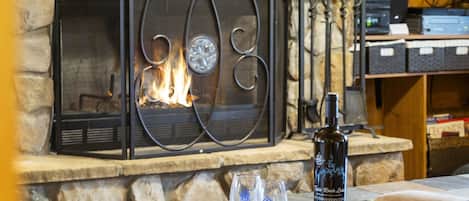 A fireplace with a stone surround, a bottle of wine, and two glasses on a table.