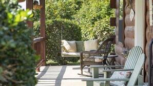 Een houten terras met twee rieten stoelen en een tafel, omgeven door weelderig groen.