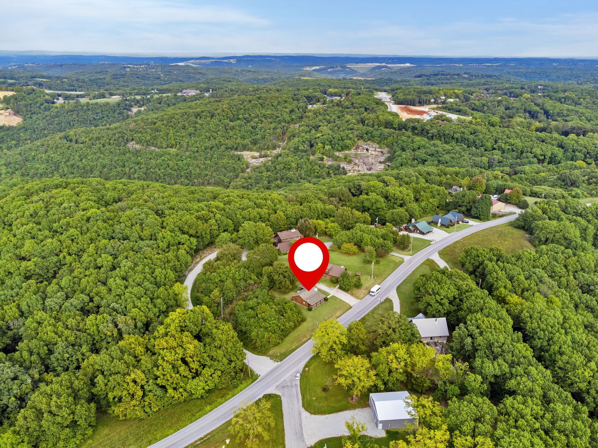 An aerial view of a rural area with dense forest, a winding road, and a few buildings.