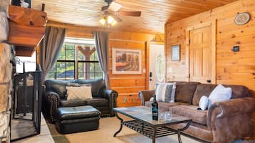A cozy cabin interior with a fireplace, leather sofas, a coffee table, and a wooden ceiling.