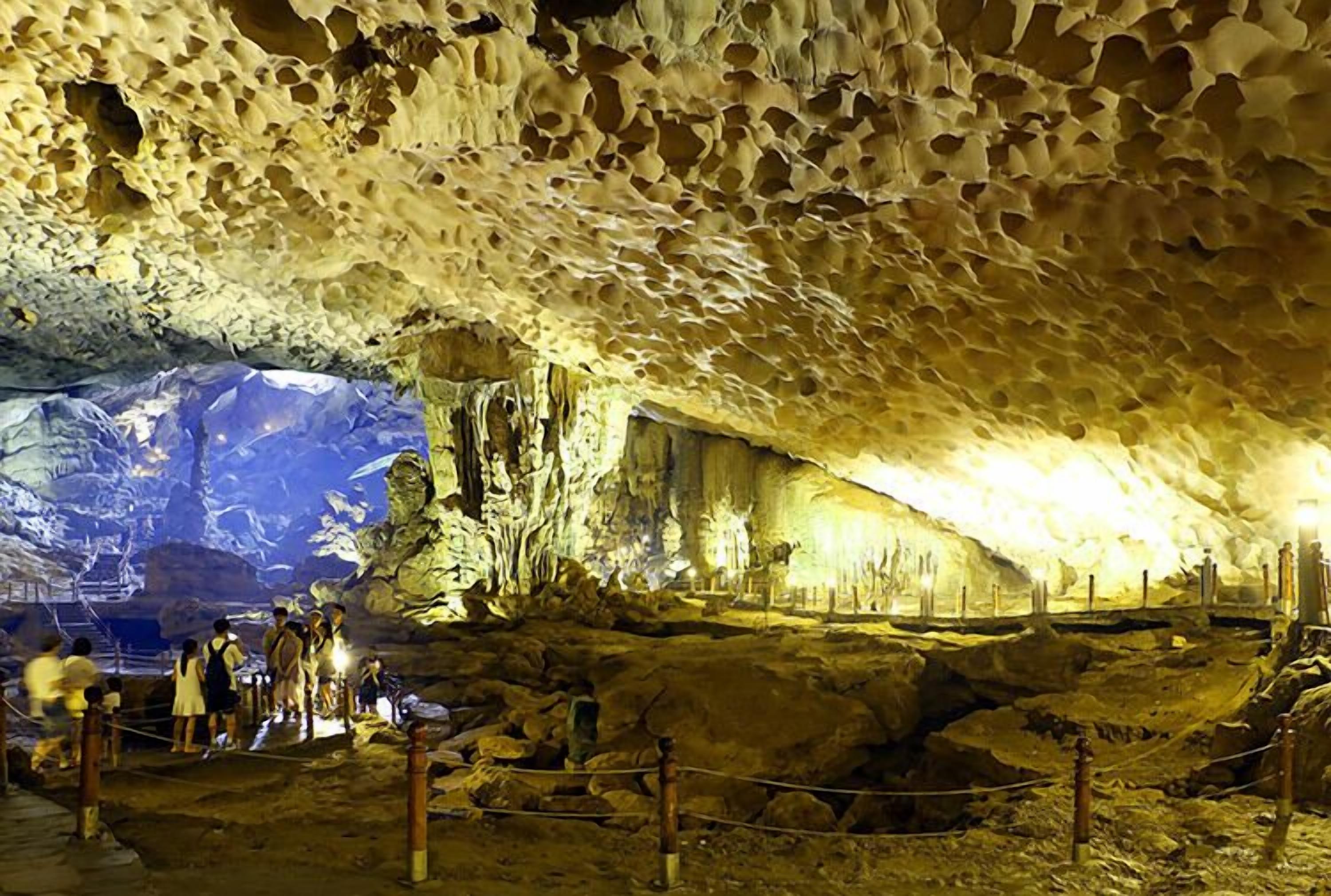 A cave interior with stalactites and stalagmites, ropes for safety, and visitors exploring.