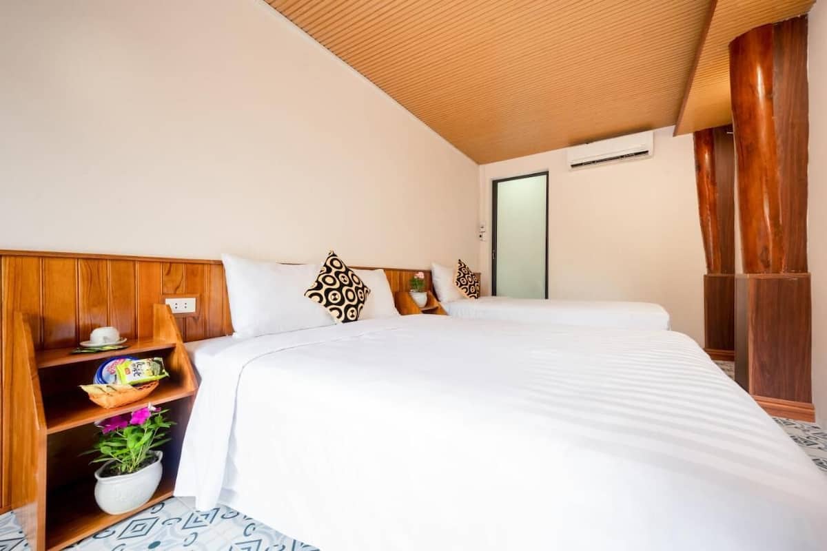 Una habitación de hotel con cabecera de madera, una cama grande con ropa de cama blanca, un estante con objetos decorativos y una planta en maceta.