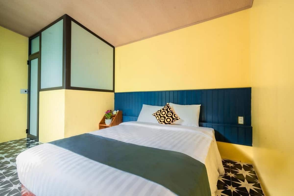 Una habitación de hotel con una cama, una mesita de noche, una planta en maceta y una ventana con persianas.