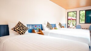 A hotel room with two beds, patterned pillows, a wooden ceiling, and large windows with a view of greenery.