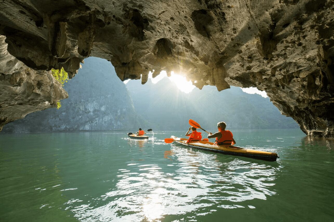 A cave with a water body inside, kayaks, and people kayaking.