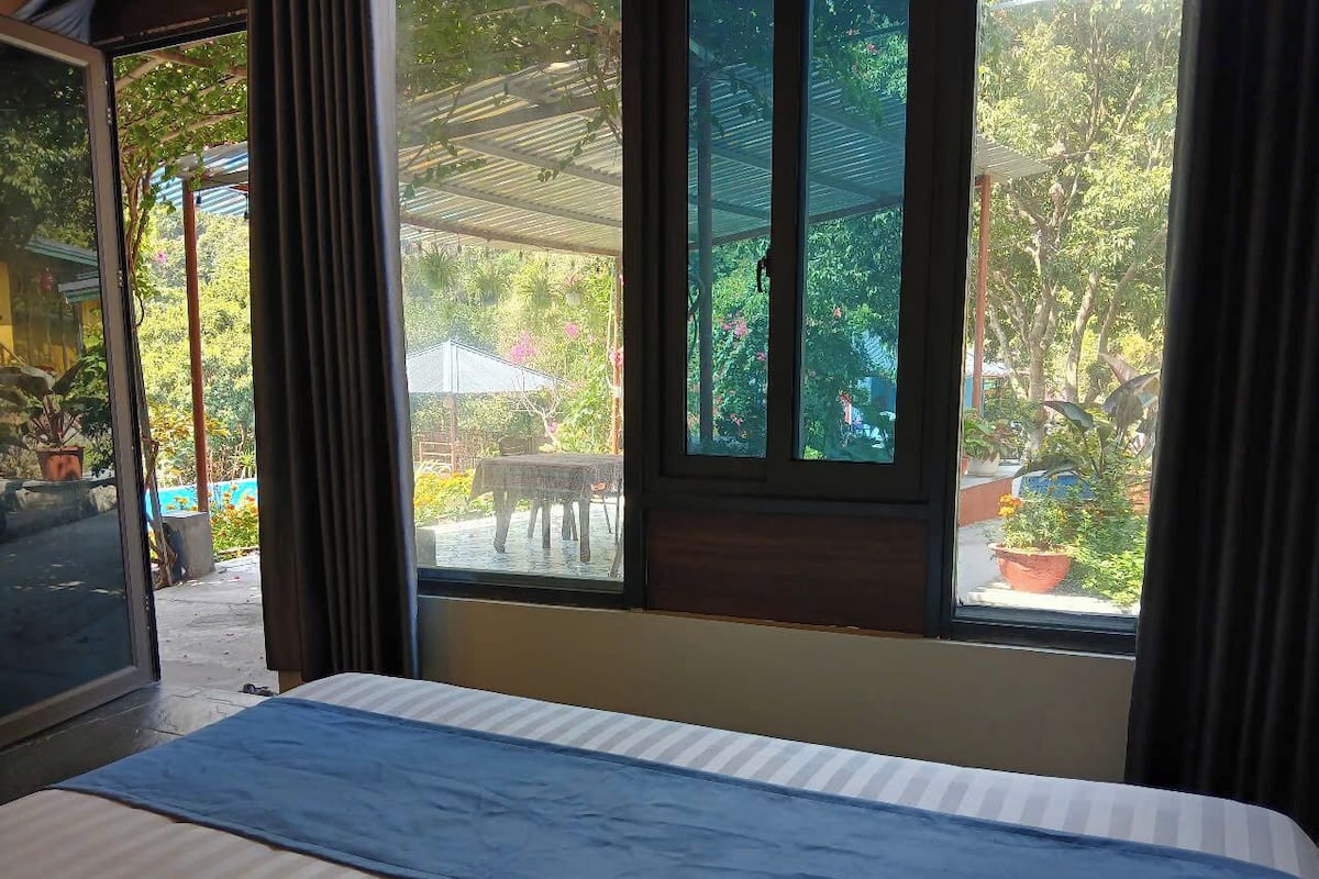 Una habitación con cama, ventana con cortinas y vistas al jardín exterior.