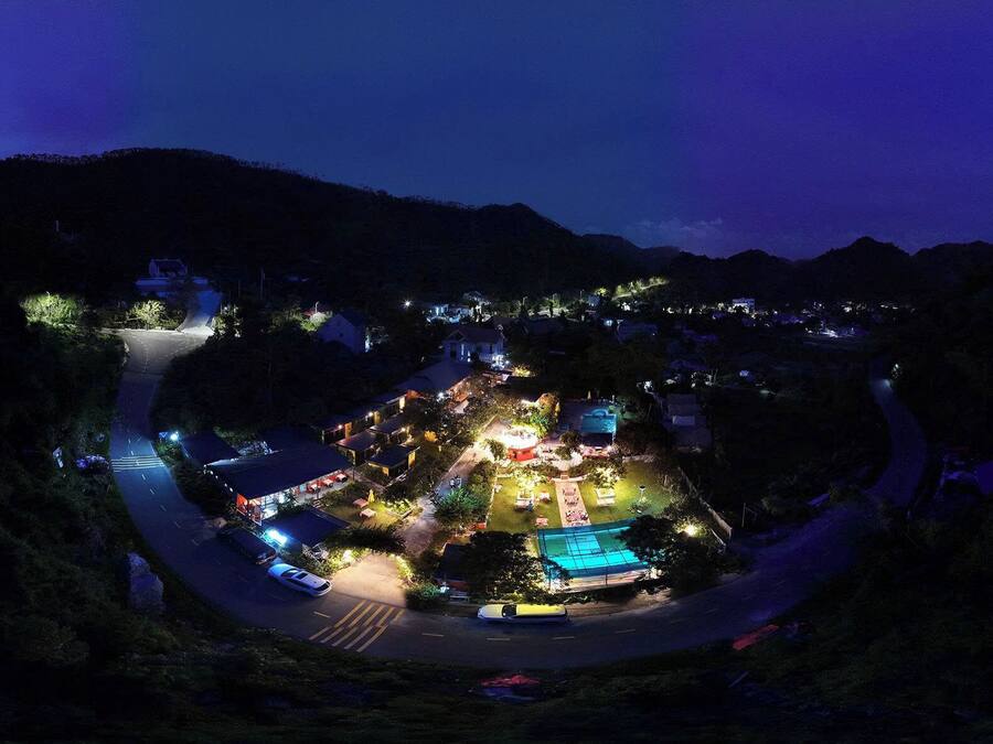 Vista noturna de um resort, com uma estrada sinuosa, edifícios iluminados e área de piscina.