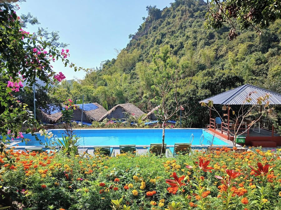 Ein Poolbereich mit Liegestühlen, einer strohgedeckten Struktur und einer Hügelkulisse mit dichter Vegetation.
