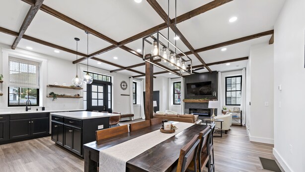 Une cuisine spacieuse avec une longue table en bois, des meubles de couleur sombre et un luminaire suspendu moderne.
