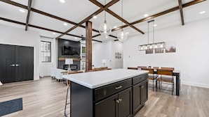 Une cuisine spacieuse dotée d’un grand îlot central, de meubles de rangement aux couleurs sombres et de poutres en bois au plafond.