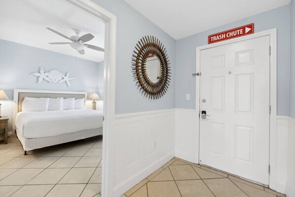 A bedroom with a bed, a ceiling fan, a wall-mounted starfish decoration, a circular mirror, and a door with a trash chute sign. - Ocean Views-14th Floor at Laketown Wharf 1404 (Panama City Beach)