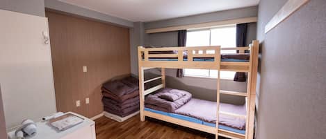 Dormitorio con literas, luz de techo, suelo de madera y ventana con cortinas.