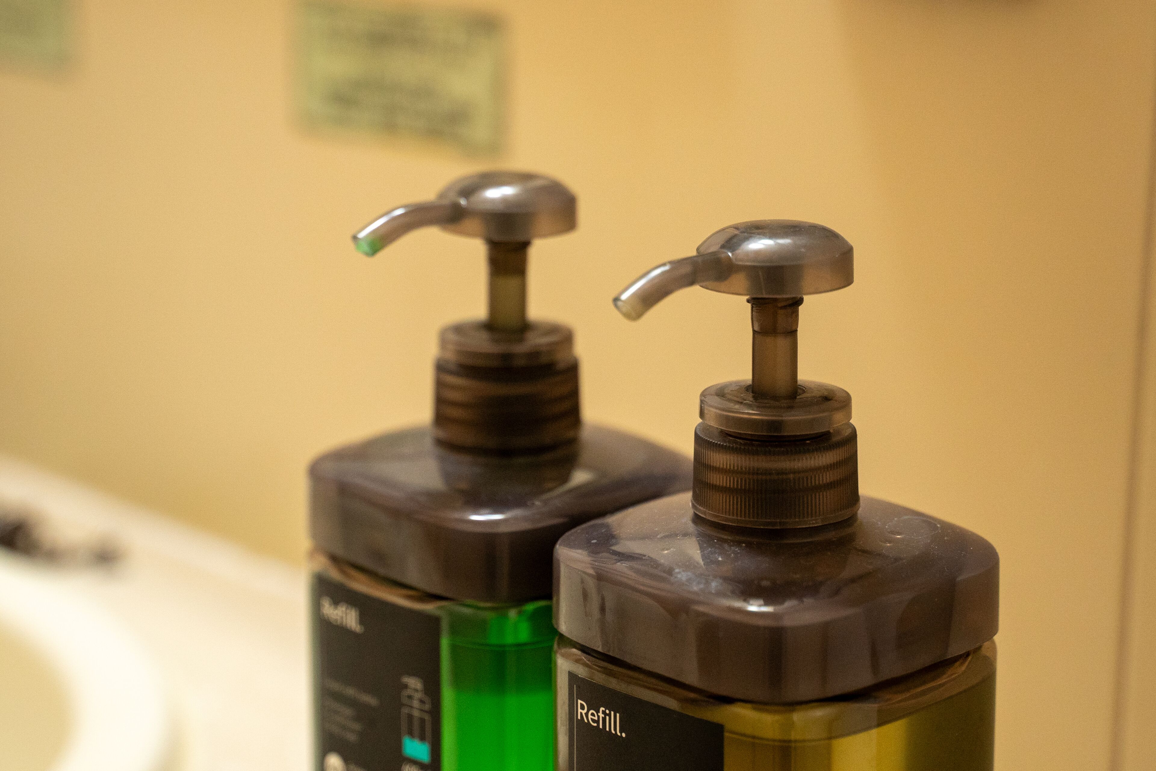 Deux distributeurs de produits d’hygiène situés dans les toilettes, chacun portant une étiquette indiquant « Recharger ».