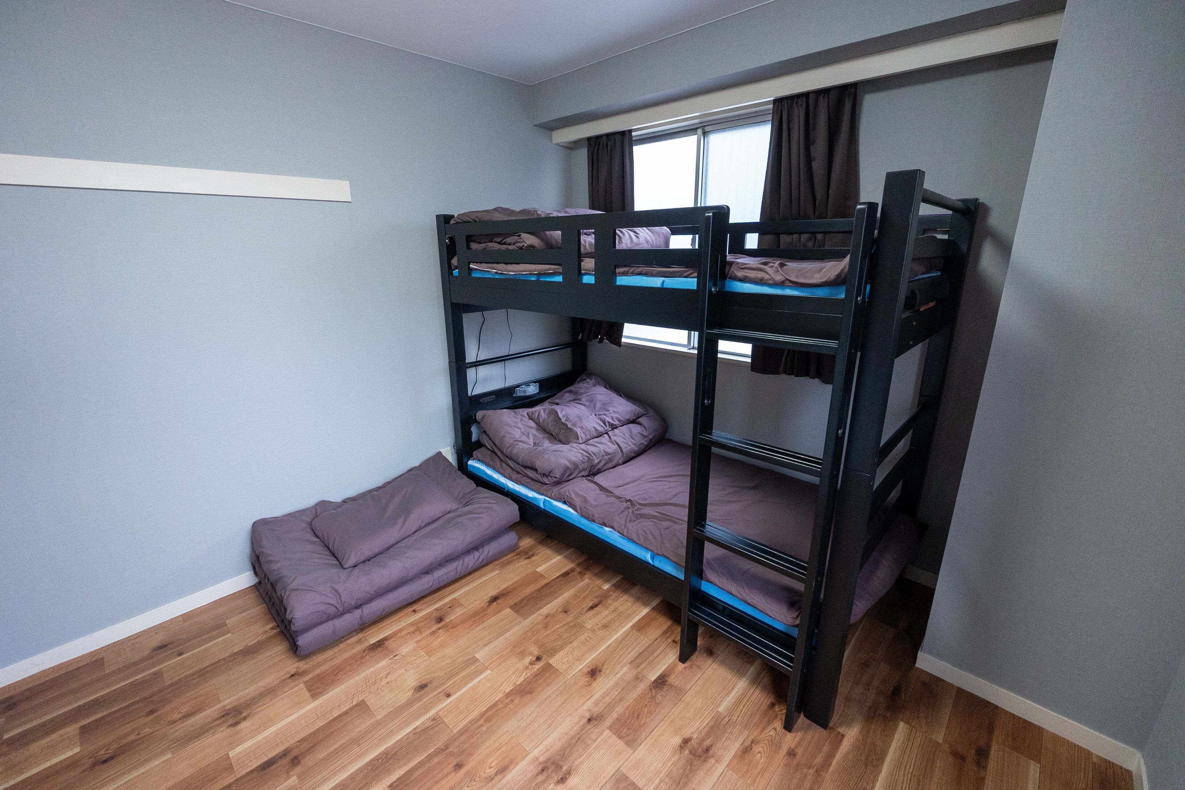 A bunk bed room with a wooden floor and a window with curtains.