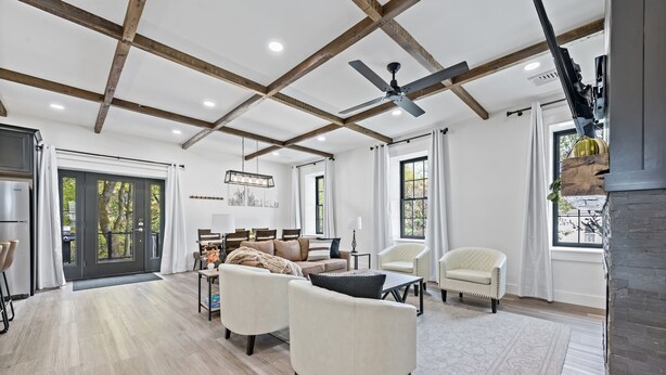 A spacious living room with a high ceiling, wooden beams, a ceiling fan, and a fireplace.