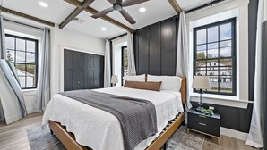 A modern bedroom with a large bed, a ceiling fan, and a view of a building through a window.