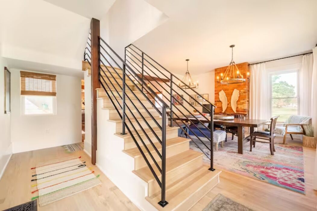 Un interior moderno con una escalera de madera, un comedor y un ventanal grande.