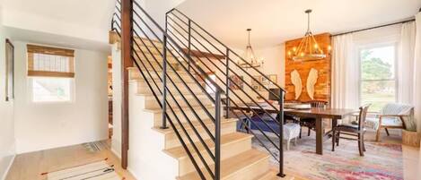 Un interior moderno con una escalera de madera, un comedor y un ventanal grande.