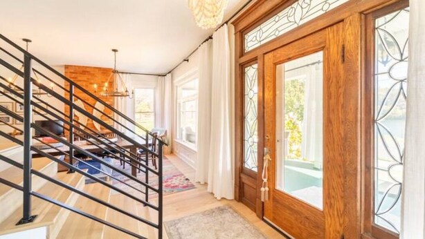 Una escalera con detalles de madera y barandillas metálicas, que conduce a un espacio con una puerta de madera grande y un ventanal con diseño geométrico.