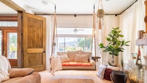 Una habitación acogedora con suelo de madera, un sofá color beige, una silla colgante tipo hamaca y un ventanal con cortinas.