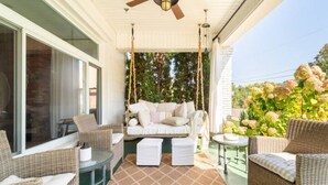 Un patio techado con mobiliario de mimbre, una hamaca y una mesa de vidrio.