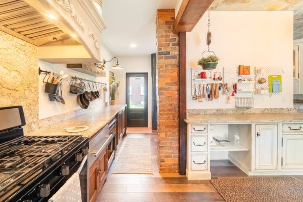 A kitchen with a gas stove, white cabinets, and a brick accent wall.