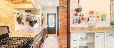 A kitchen with a gas stove, white cabinets, and a brick accent wall.