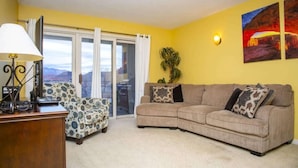 A living room with a sofa, armchair, lamp, and a view through a glass door.