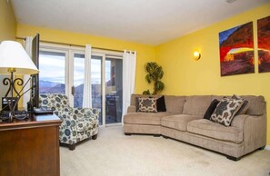 Un salón con sofá, sillón, lámpara y vistas a través de un ventanal.
