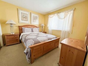 A bedroom with a wooden bed, two bedside tables, a nightstand, a dresser, and a window with curtains. - Las Palmas Resort #107 | All-Inclusive Amenities (Saint George)
