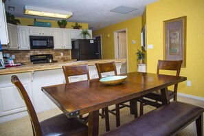 Un comedor con una mesa y sillas de madera, una cocina al fondo y una pared amarilla.